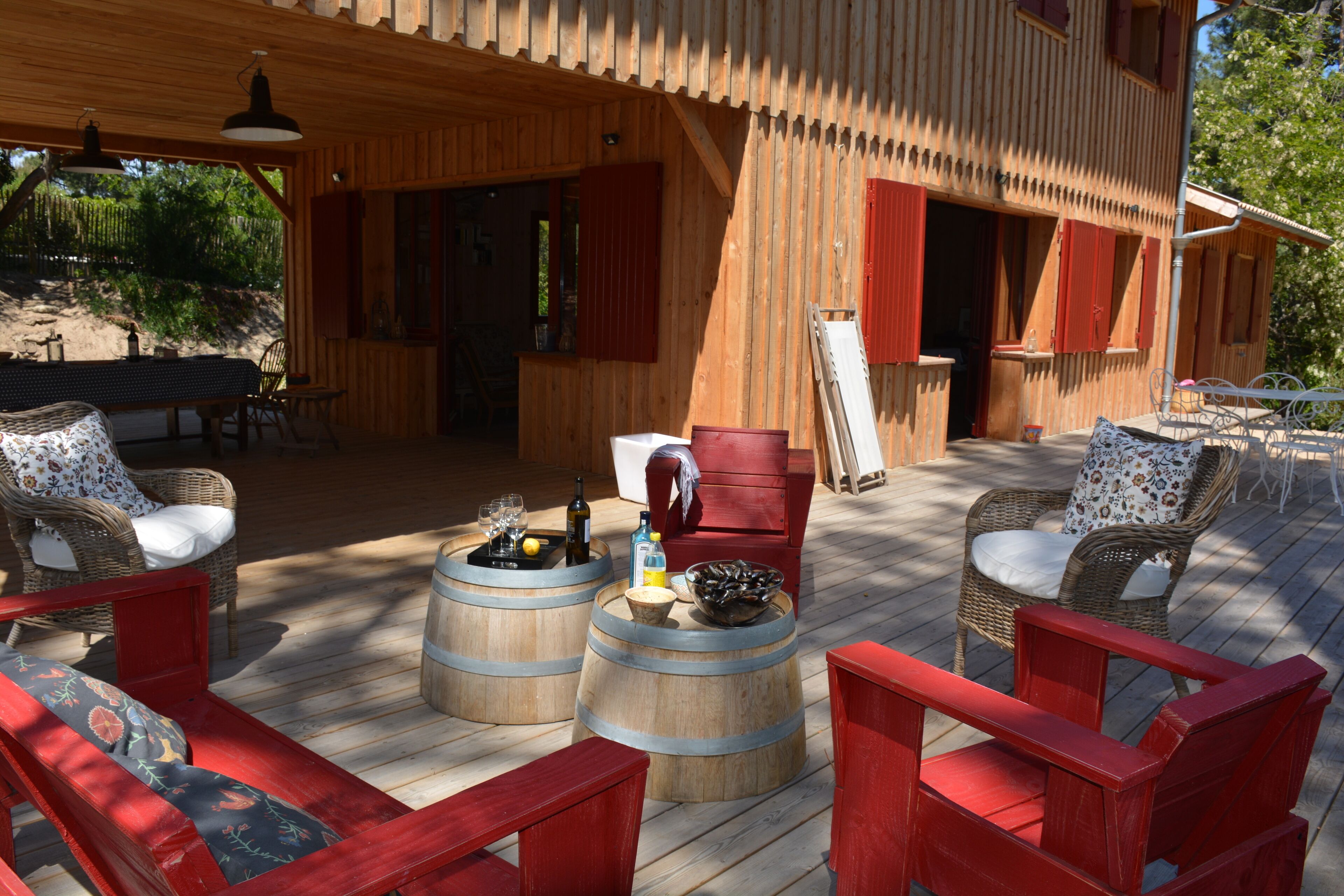 A wooden deck with red furniture, including chairs and a bench, and two wooden barrels with items on them.