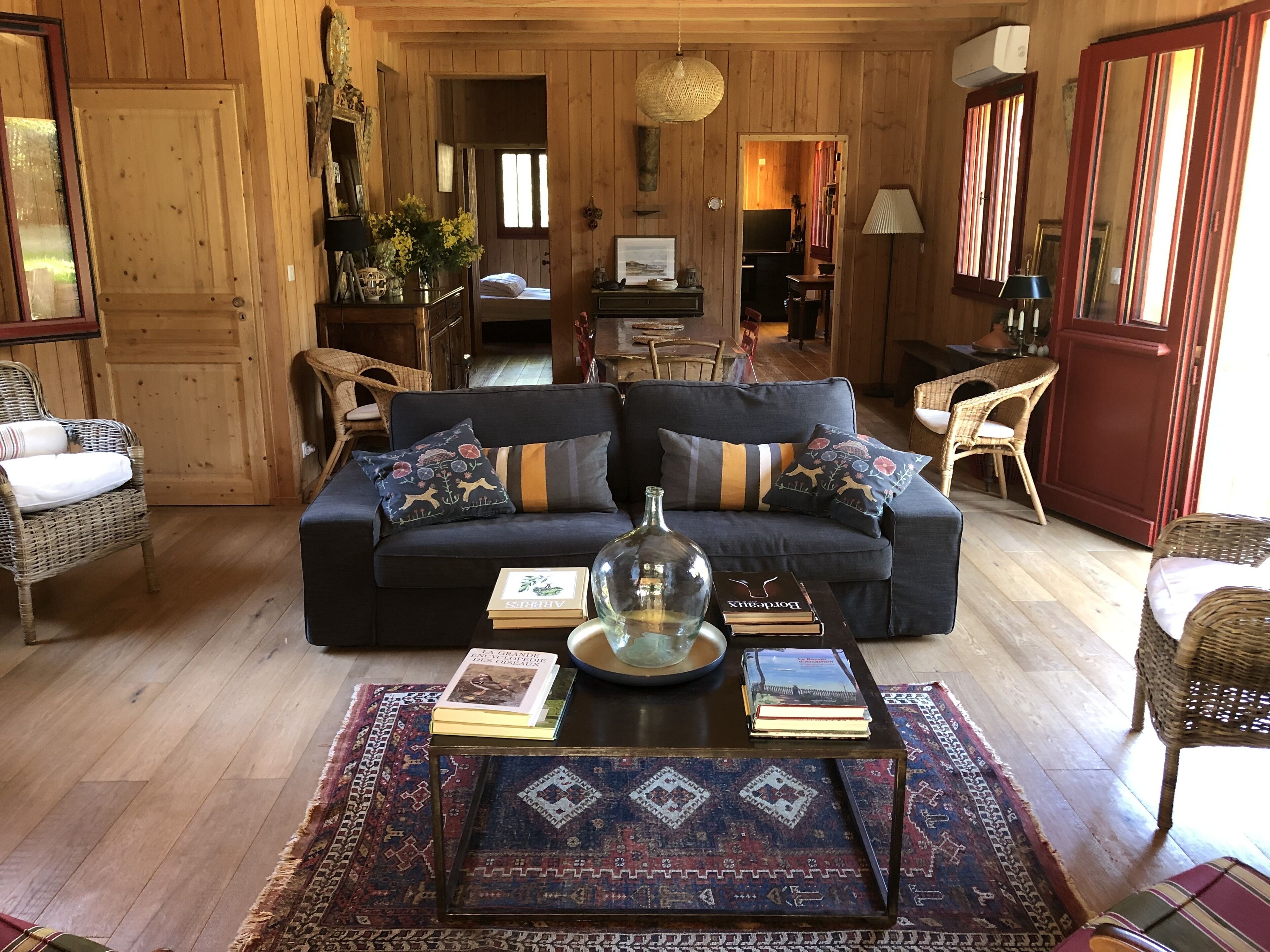 Ein gemütliches Wohnzimmer mit einem dunkelblauen Sofa, Korbstühlen, einem Couchtisch mit Büchern und einem gemusterten Teppich.