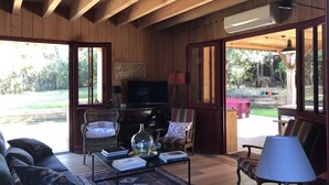 Una sala de estar acogedora con techo de madera, televisor, muebles de mimbre y vistas al exterior.