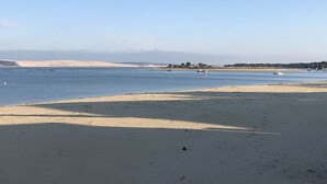 Una playa con cielo despejado, agua tranquila y dunas al fondo.