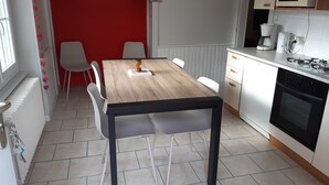 A compact kitchen with a wooden table, white chairs, a white stove, and a red wall. - House 150m apartment in the city center, in a very quiet place (Gérardmer)