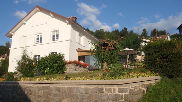 A two-story house with a stone wall in front, surrounded by greenery and flowers. - House 150m apartment in the city center, in a very quiet place (Gérardmer)