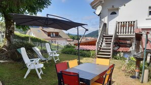 A patio with a table and chairs, a large umbrella, and a view of houses and a hill in the background. - House 150m apartment in the city center, in a very quiet place (Gérardmer)