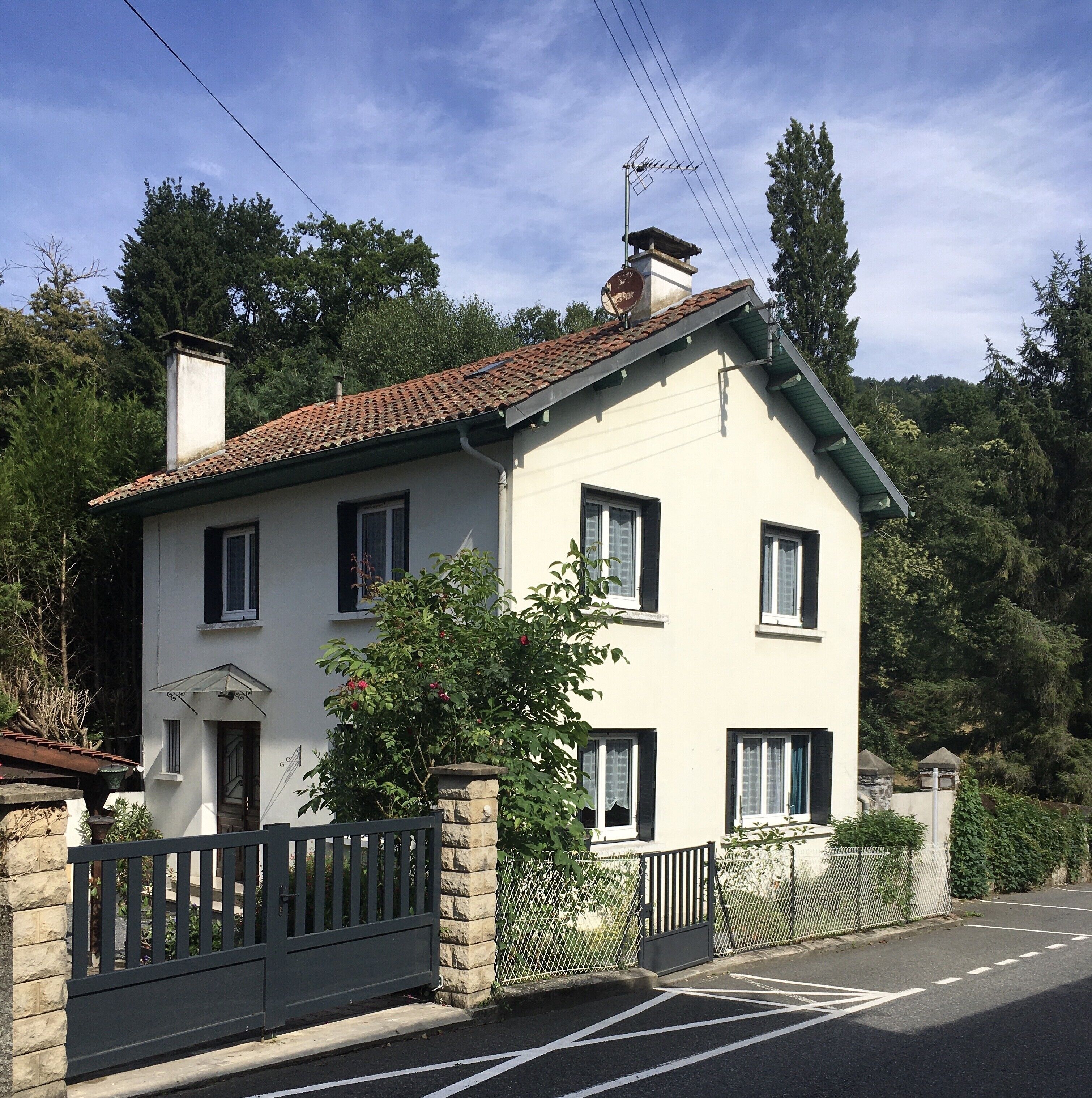 A two-story house with a tiled roof, a chimney, and a small garden with a fence.