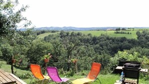 Eine Terrasse mit Tisch und drei Stühlen, mit Blick auf ein üppiges Tal mit Bäumen und weit entfernten Hügeln.