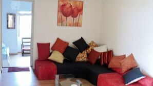 Ein Wohnzimmer mit einem roten Sofa, einem Glastisch und einem Blumenbild an der Wand.