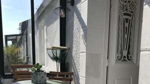 A sunlit patio with a table and chairs, a decorative door, and a window with a view of the street.