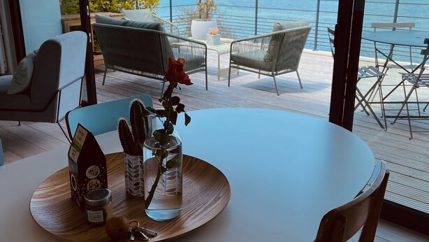 A round dining table with a wooden tray, a glass vase with a red rose, and a small cactus plant.