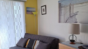 Una habitación con un sofá gris, un armario de madera, una mesa de comedor con sillas, una lámpara y un cuadro en la pared.