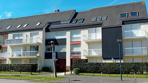 Un edificio residencial de varios pisos con balcones, un cartel de estacionamiento que indica zona de 30, y un paso de peatones.