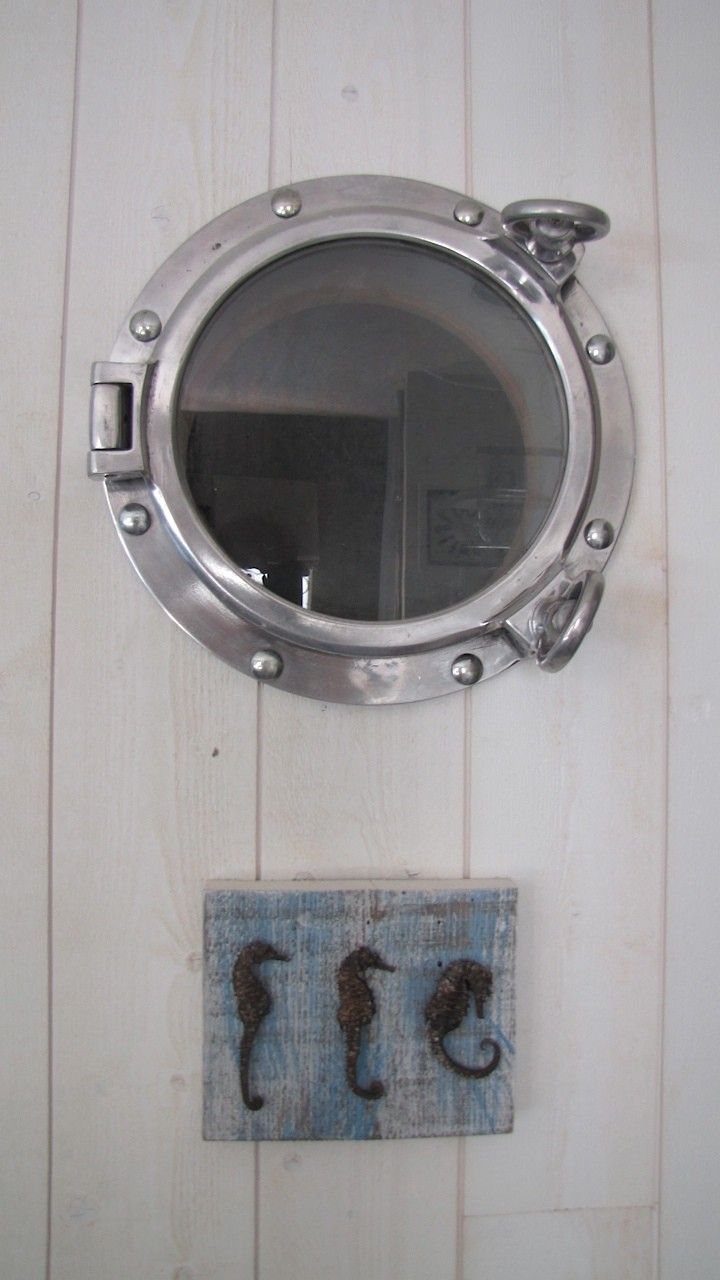 A round porthole window with a metal frame and a small door on the left side. Below it, there is a wooden panel with two seahorse designs.