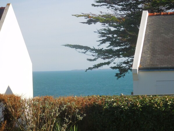 A coastal view with a clear sky, a body of water, and a building with a tiled roof.
