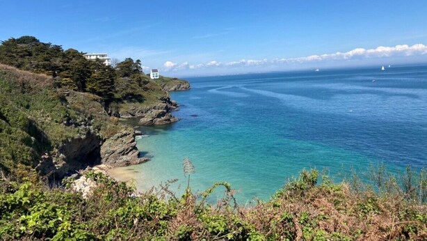 A coastal landscape with a clear view of the sea, rocky terrain, and a building on the left.