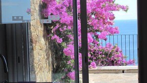 Une cuisine avec un mur en pierre et une vue sur un balcon orné de fleurs roses et donnant sur la mer.