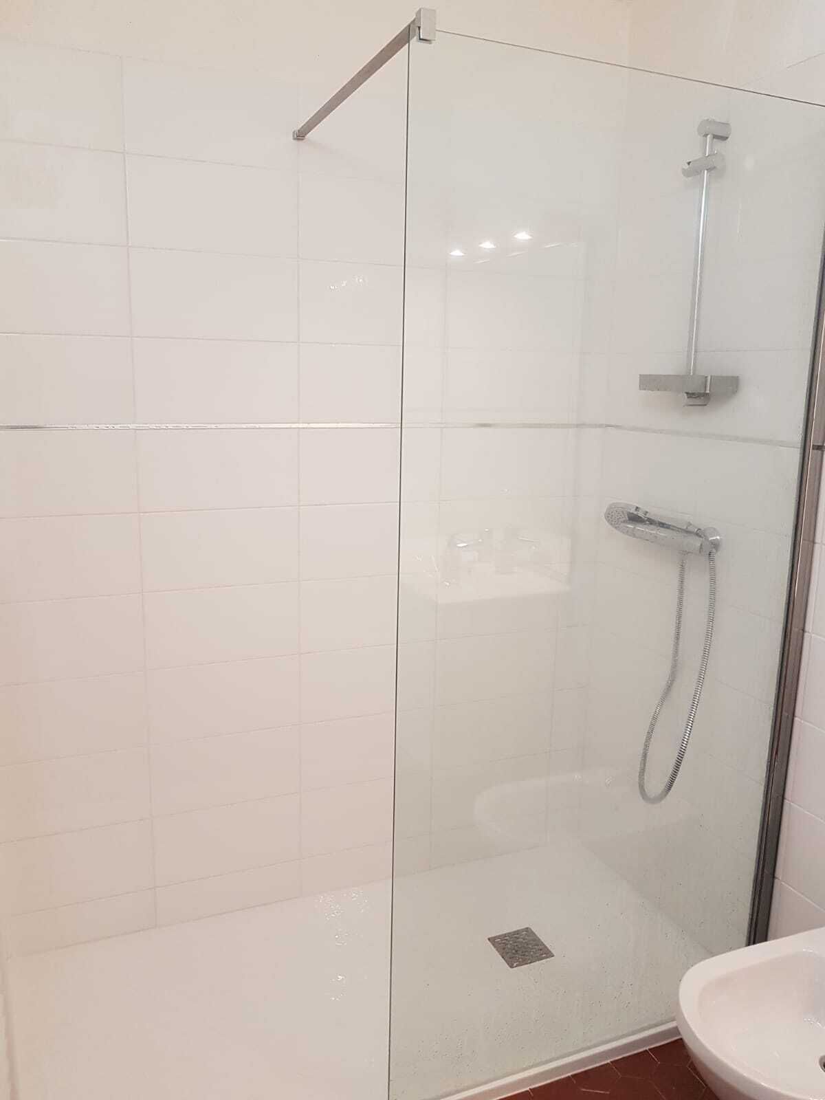 Een douchecabine met glazen wanden, een handdouche en een wandmengkraan.