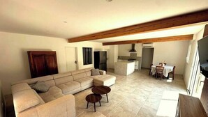 A living room with a sectional sofa, two round coffee tables, and a dining area with a table and chairs. - House surrounded by olive trees, set against a hill, on 2000 m2 of quiet land (Ceyreste)