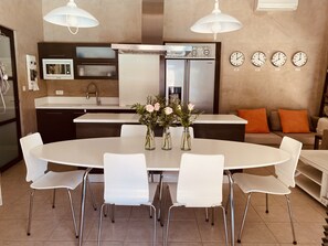 A modern kitchen with a dining area, white chairs, a round table, and a refrigerator.