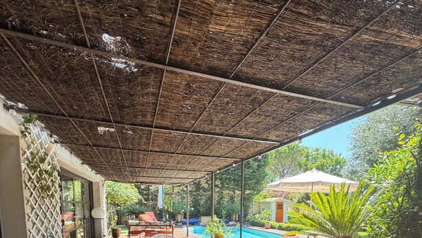 Eine Holzterrasse mit Korbstühlen, einem Pool und Kübelpflanzen.