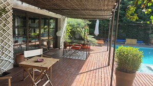 Eine Holzterrasse mit Tisch und Stühlen, einer überdachten Sitzecke und einem Pool.