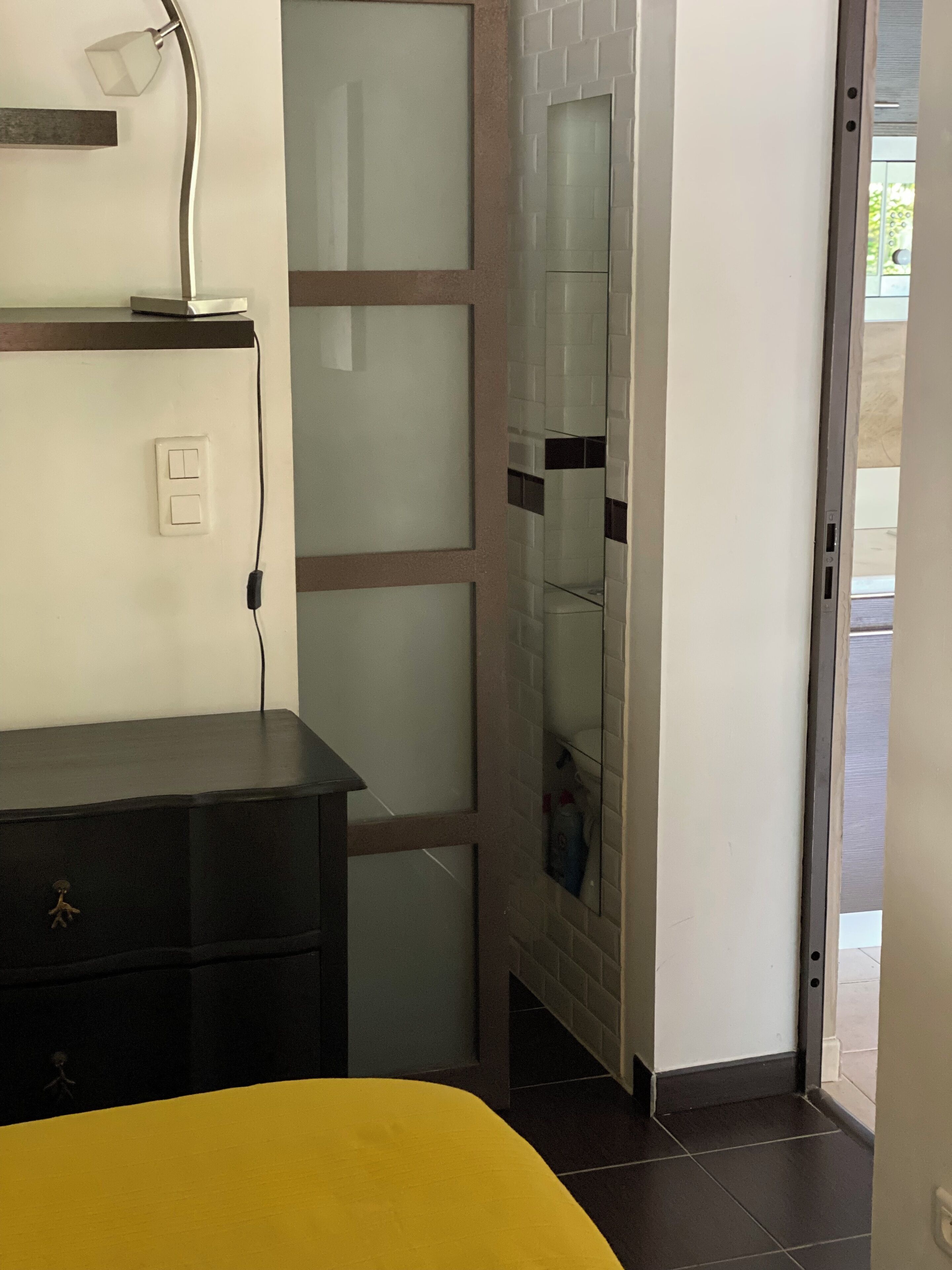 A room with a bed, a dresser, a lamp, and a glass door leading to a balcony.