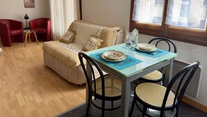 A cozy living room with a sofa, a dining table set for two, and a red chair.