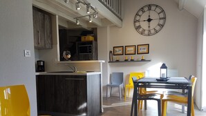 A modern kitchen with a central island, a dining area with yellow chairs, and a large wall clock. - A stay by the lake ... (Génos)