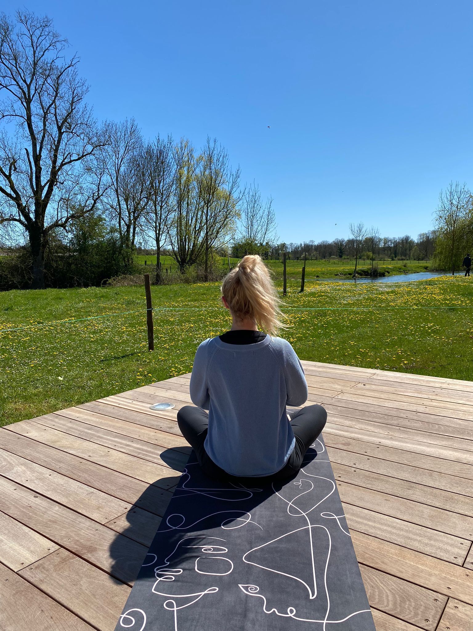 A person sitting on a wooden deck outdoors with a clear view of a river and trees in the background.