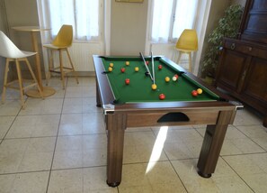 A pool table with balls, two yellow chairs, and a lamp in a room with tiled flooring.