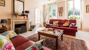 A living room with a fireplace, a red sofa, a coffee table, and a large window with a view of trees.