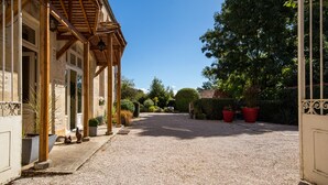 A gravel driveway leading to a building with a wooden pergola and potted plants.