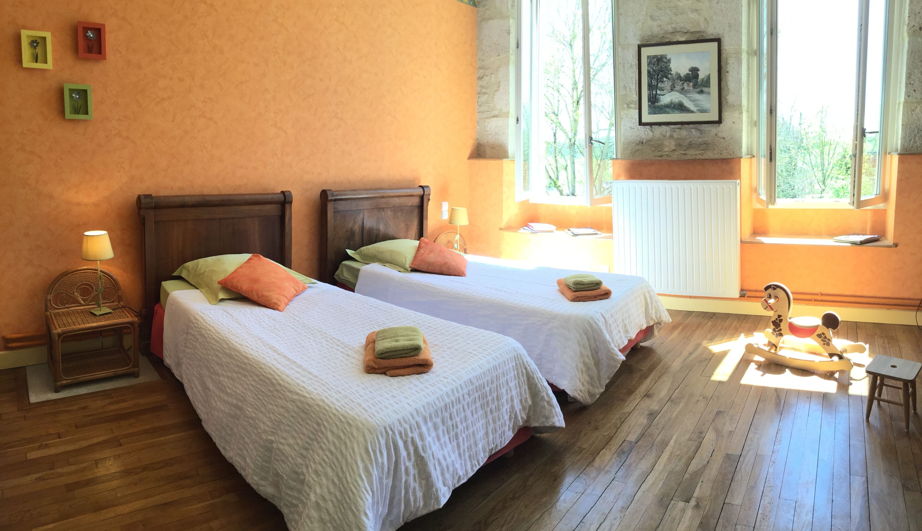 Una habitación con dos camas, pisos de madera, un ventanal con vistas y un radiador.