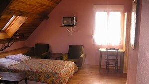 A cozy room with two beds, a small table, a chair, and a television on a stand. - large capacity village house (LARUNS)