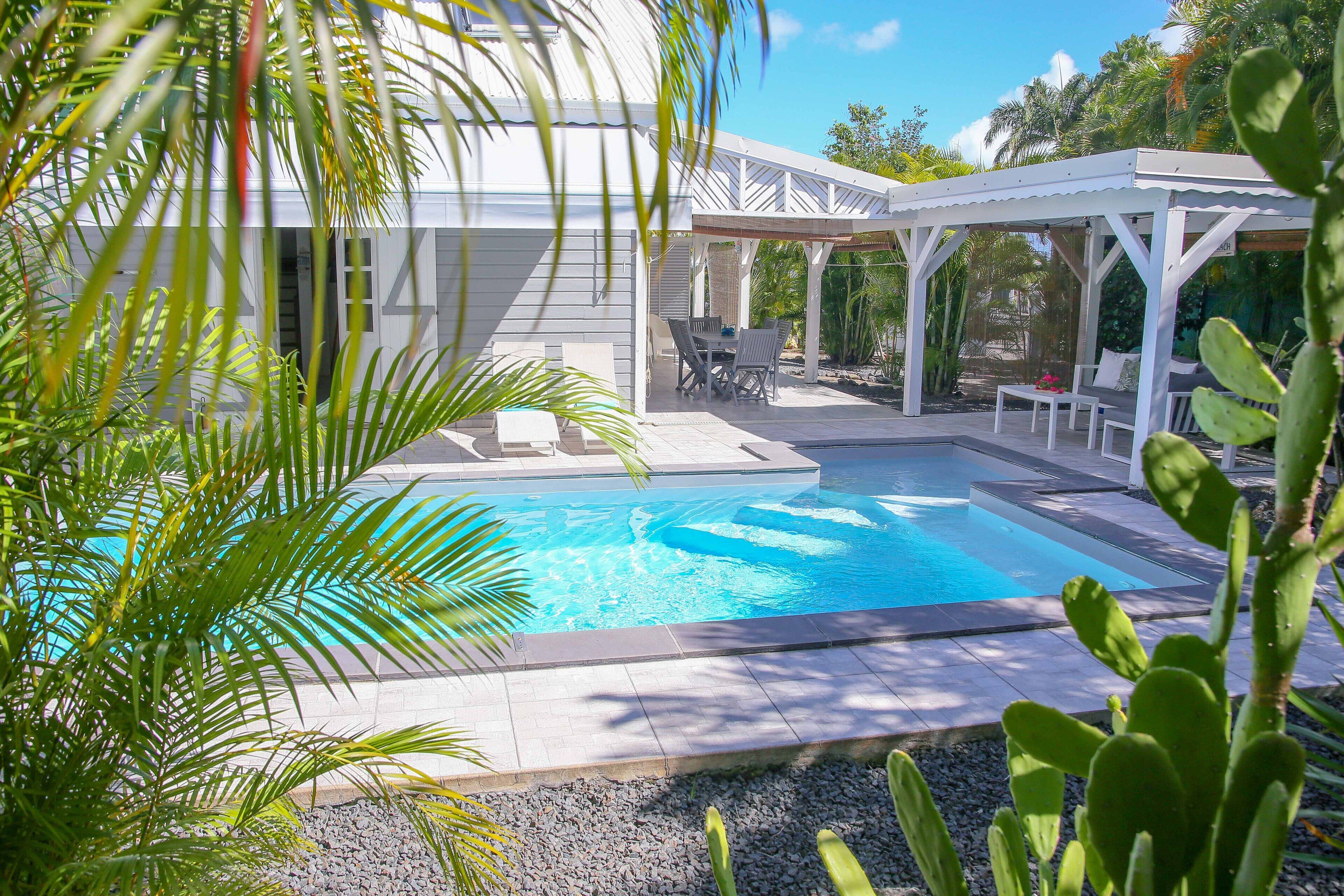 Un espace piscine doté d’un patio couvert, de chaises longues et d’une pergola.