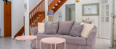 A living room with a sofa, two small tables, a patterned rug, a wooden staircase, and a door with a mirror.