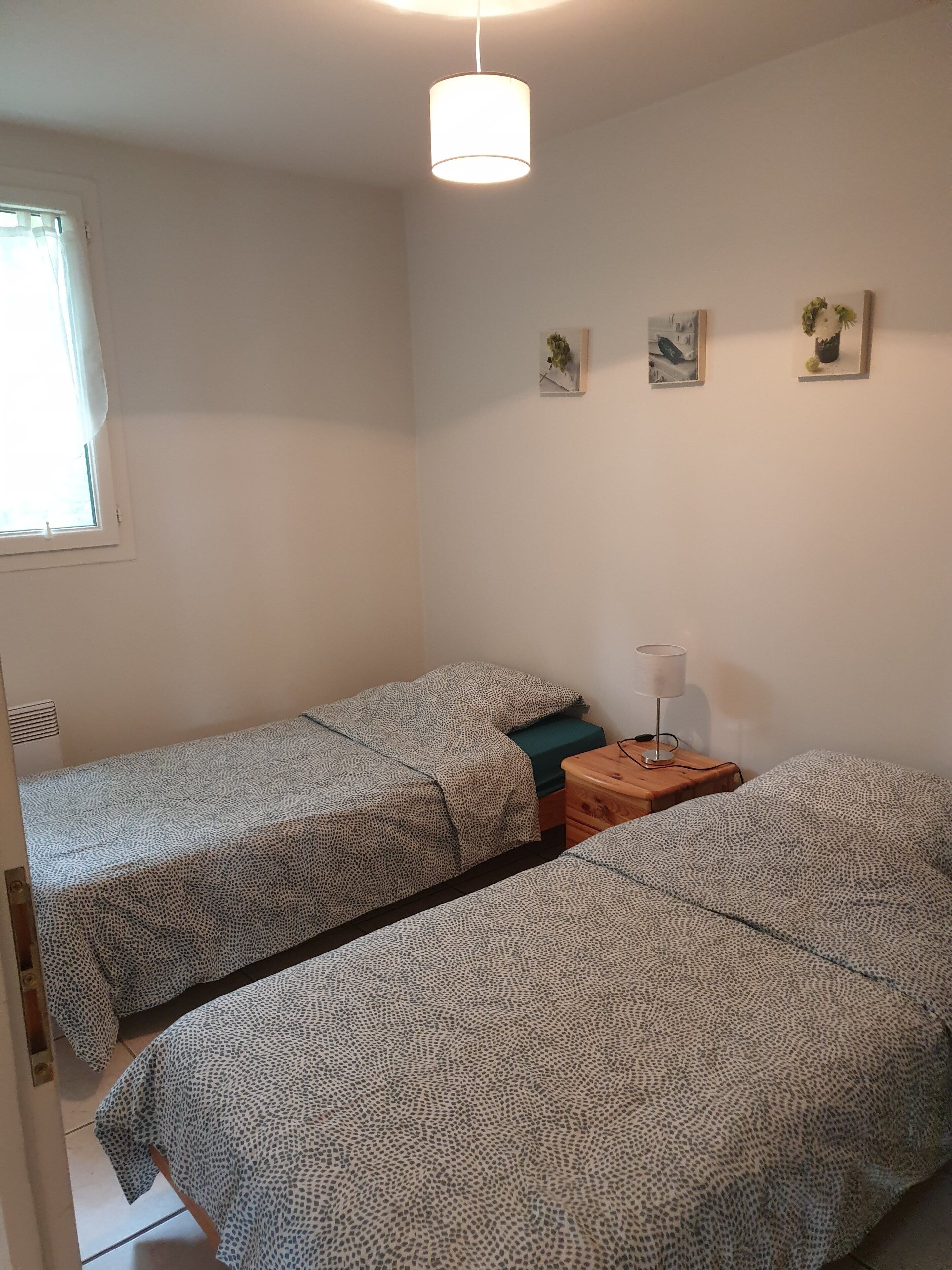 A room with two beds, a small table with a lamp, and a window with curtains.
