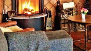 Een gezellige woonkamer met een houtkachel, een comfortabele bank en een eettafel met stoelen.