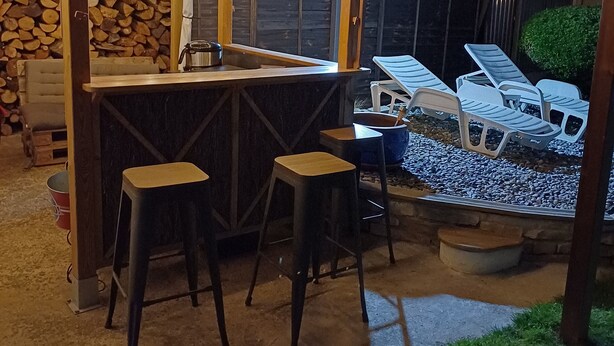 An outdoor bar area with a wooden structure, bar stools, and a seating area with lounge chairs.