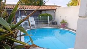 A swimming pool surrounded by a white fence, with a tiled roof and a potted plant nearby.