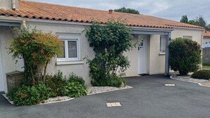 A two-story building with a tiled roof, a small garden with various plants, and a paved driveway.