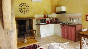 A compact kitchen with a microwave, stove, and sink. There is a wooden table and a chair, and a clock on the wall.