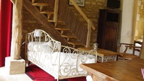 A rustic room with a stone wall, wooden staircase, a bed, a wooden dining table, and a TV.