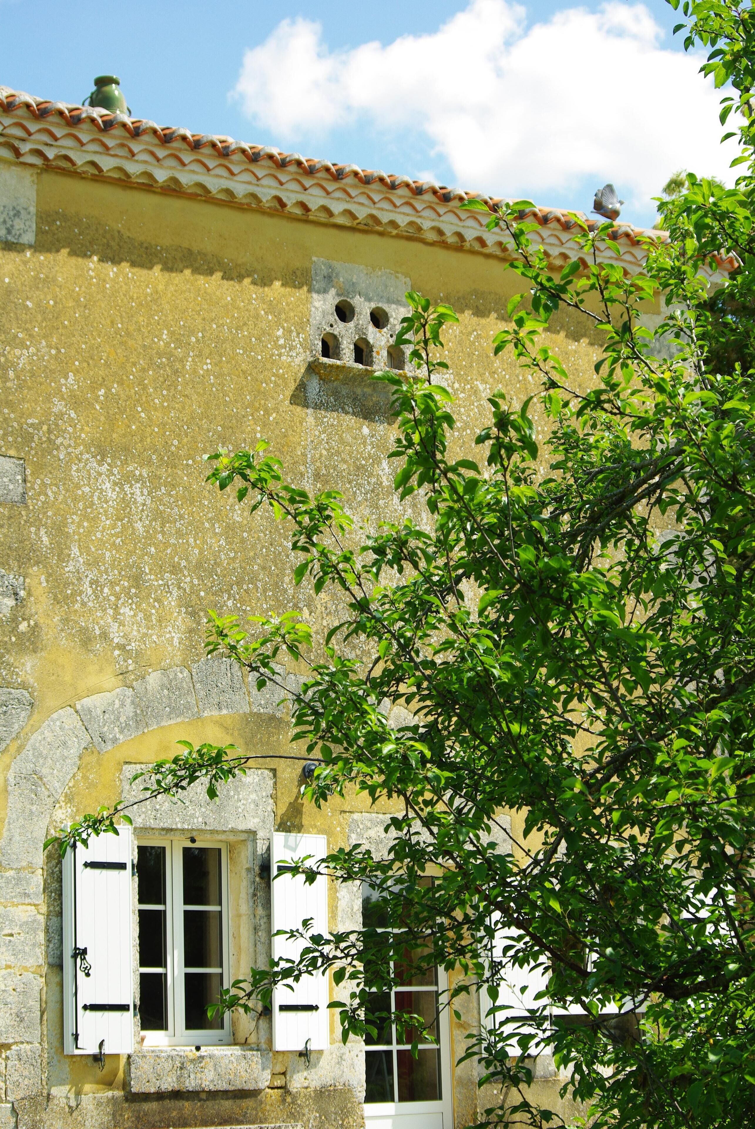 Un bâtiment à la façade jaune, doté d’un toit en tuiles et d’une fenêtre avec des volets.