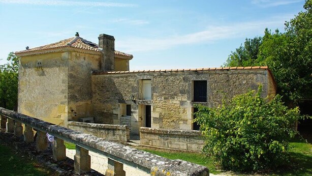 A stone building with a tiled roof, a small window, and a stone staircase leading to a door.