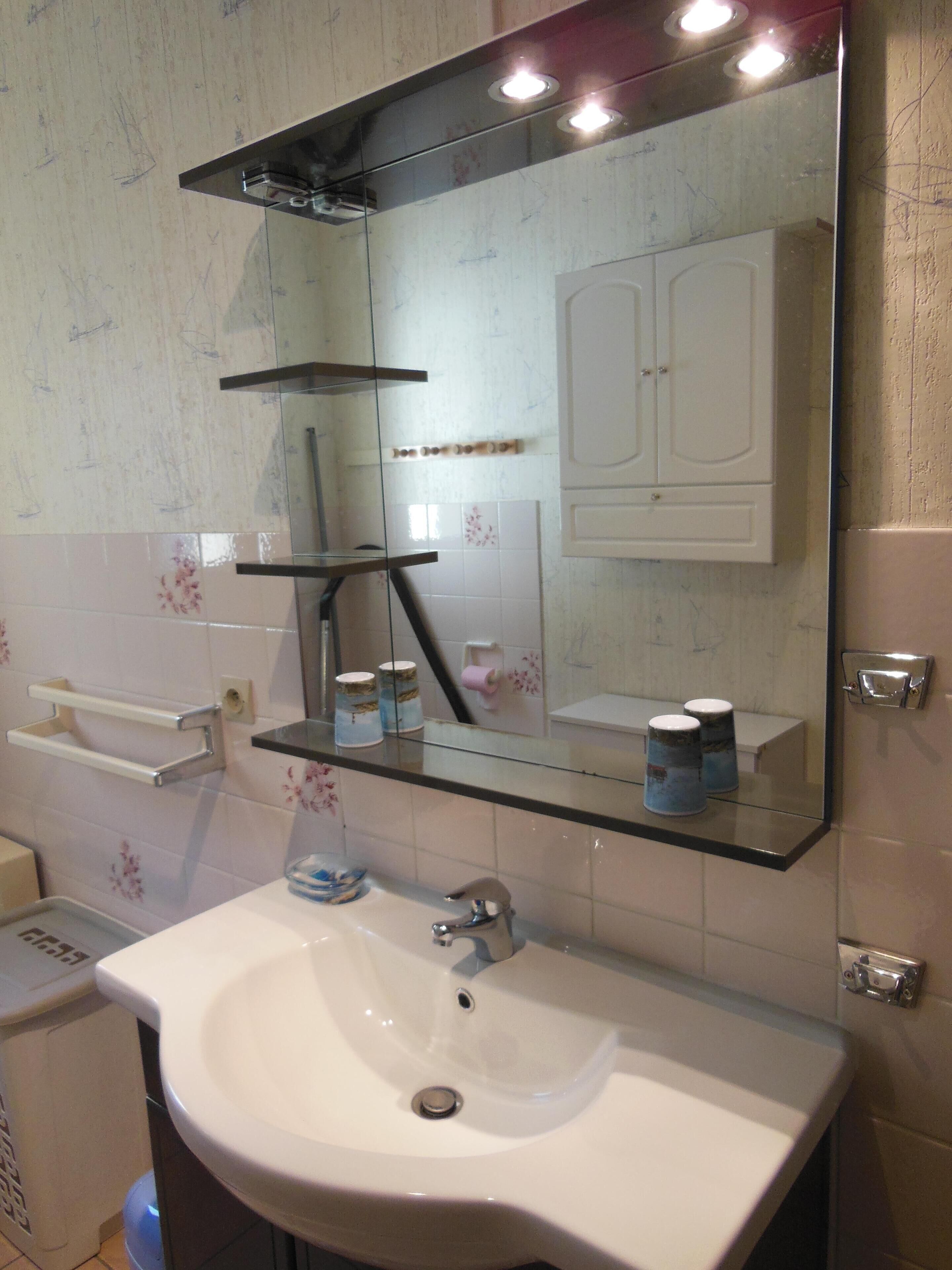 A bathroom with a white sink, a mirror, and a glass shelf above the sink.
