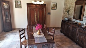 A dining room with a wooden table, chairs, a vase of flowers, a chandelier, a clock, and a stone wall. - Brittany house south Finistère, in the countryside, quiet, independent, wifi (Bannalec)