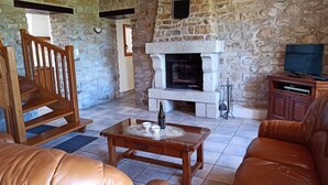 A stone-walled living room with a fireplace, leather sofas, a wooden coffee table, and a television on a wooden cabinet. - Brittany house south Finistère, in the countryside, quiet, independent, wifi (Bannalec)