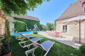 Un patio trasero con piscina, sillas de descanso, una mesa y una construcción de piedra.