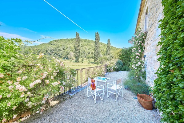 Un patio con una mesa y sillas, una cesta de mimbre y vistas a una ladera verde.