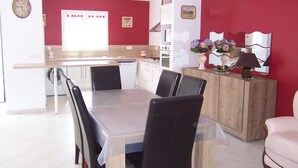 Un comedor con mesa y sillas, una cocina con pileta y placares, y una pared roja decorativa.