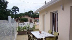 Un patio exterior con mesa y sillas, una cerca blanca y un edificio con puerta y ventanas.